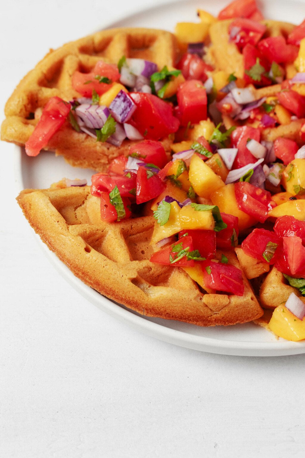 A slice of a vegan crispy cornmeal waffle has been pulled back from the waffle itself. The mixture rests on a white plate.