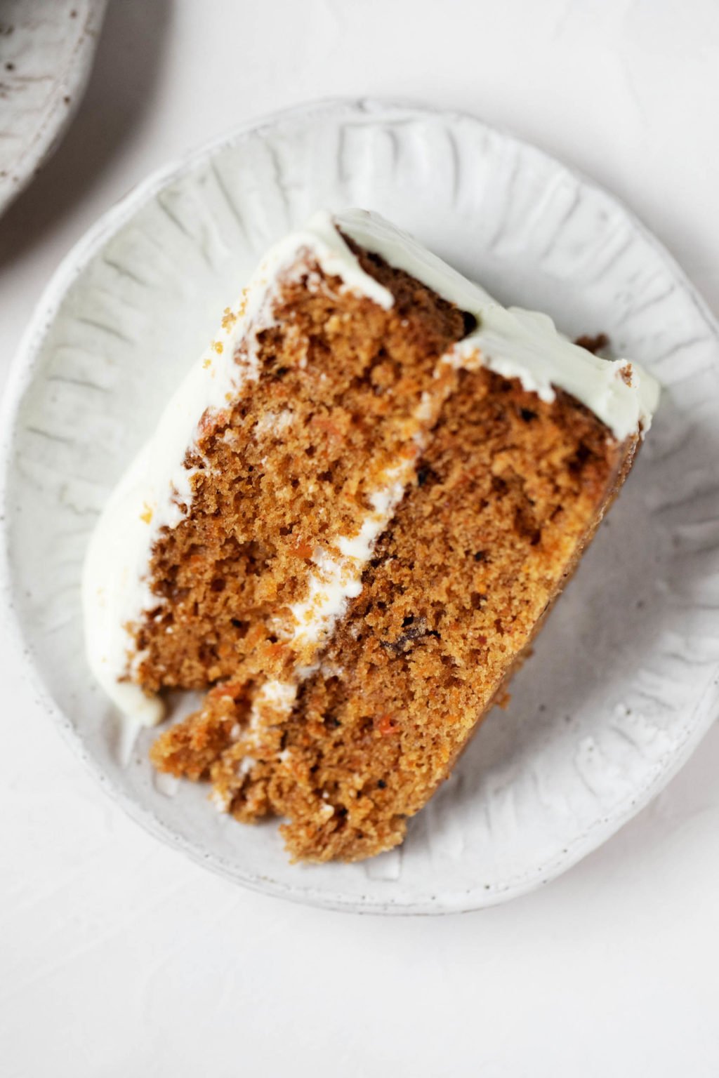 An overhead photograph of a dessert plate with a slice of vegan pumpkin carrot cake, lightly frosted with cream cheese frosting.