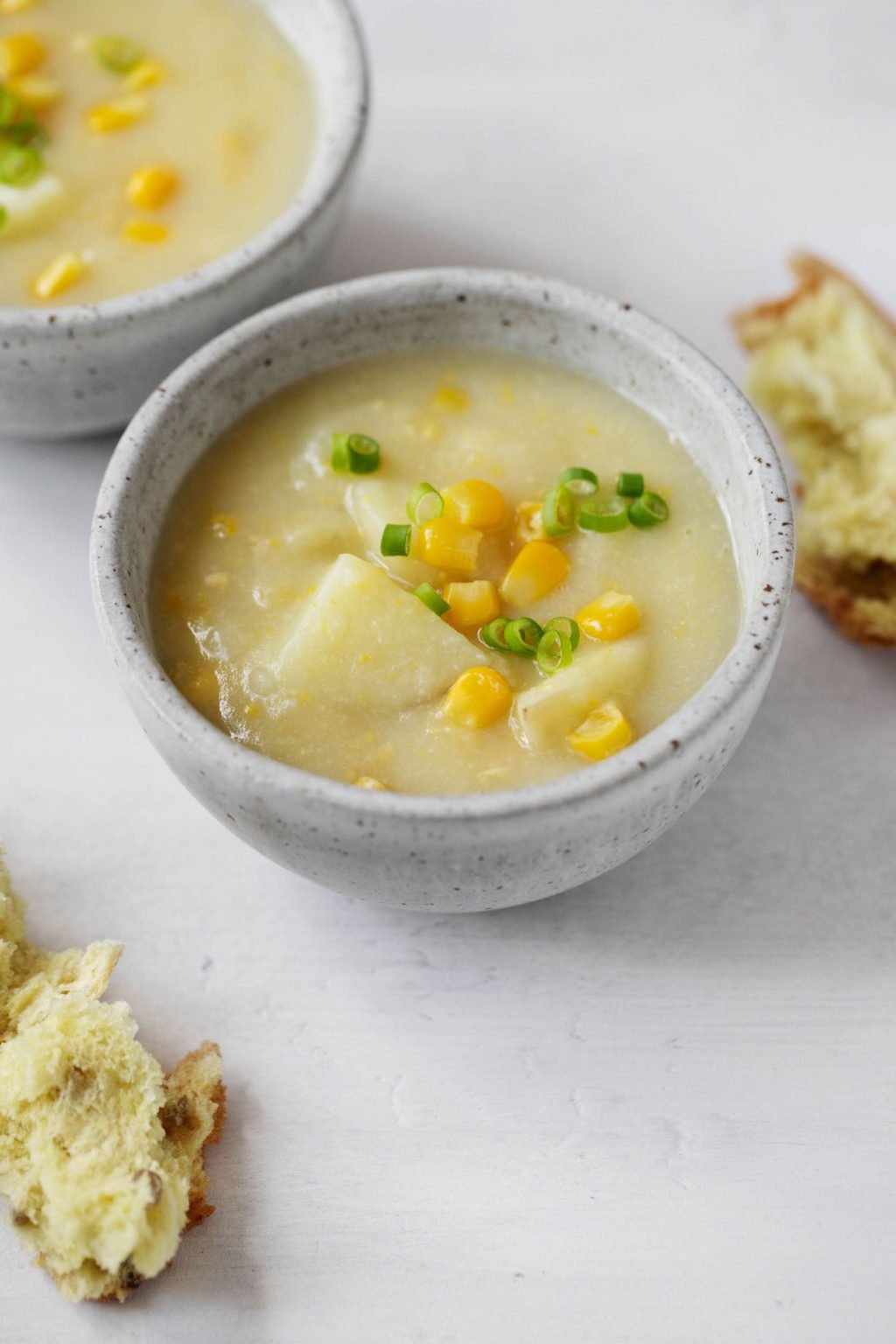 A small bowl of creamy vegan cauliflower corn chowder, topped with snipped chives and served with torn pieces of bread.