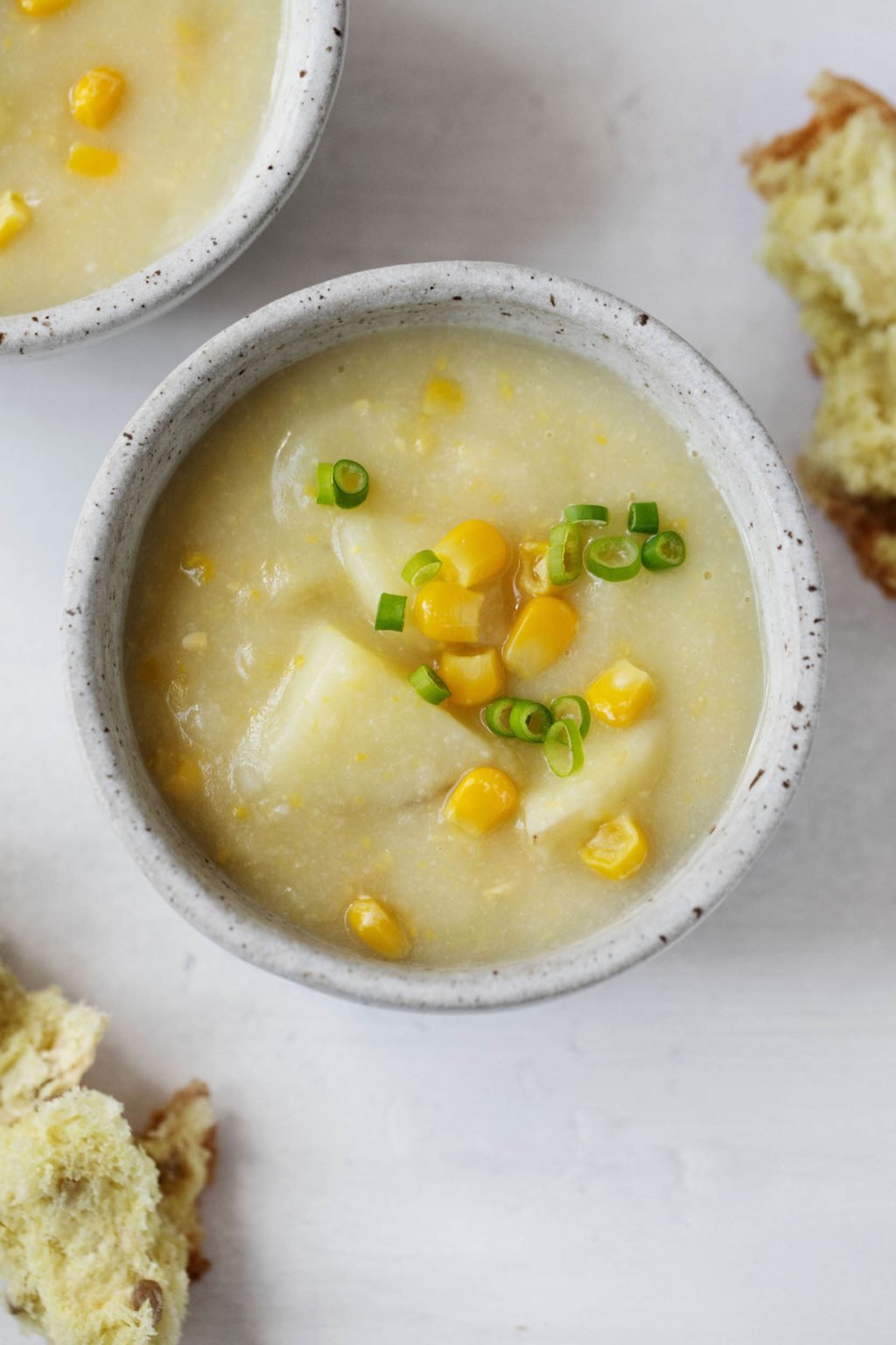 A creamy, inviting bowl of vegan chowder is topped with corn kernels and chives.