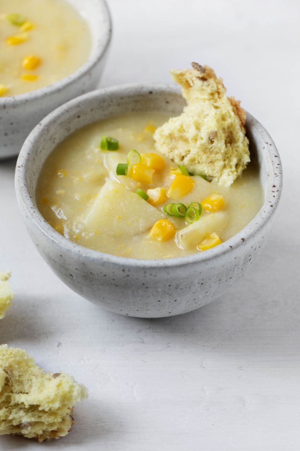 A serving bowl of vegan cauliflower corn chowder is served with a torn piece of bread dunked into the warm soup.
