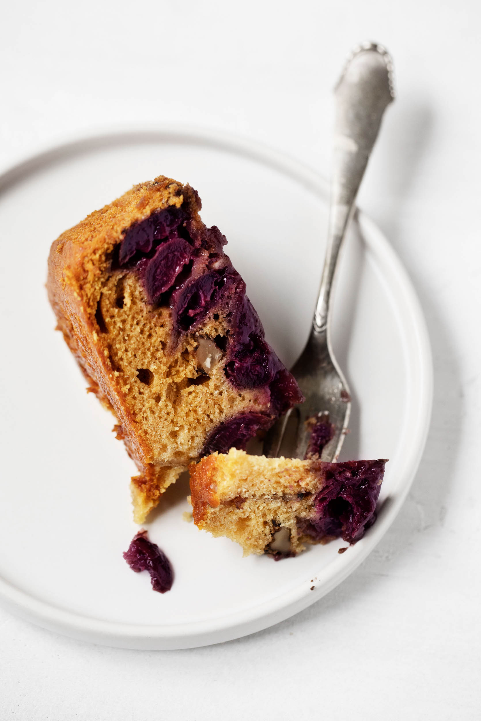 A slice of cherry cake is placed on a white dessert plate and about to be eaten.