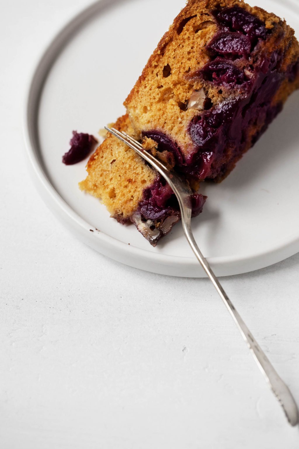 A close up photograph of a fork, slicing into a piece of fruit-filled cake.