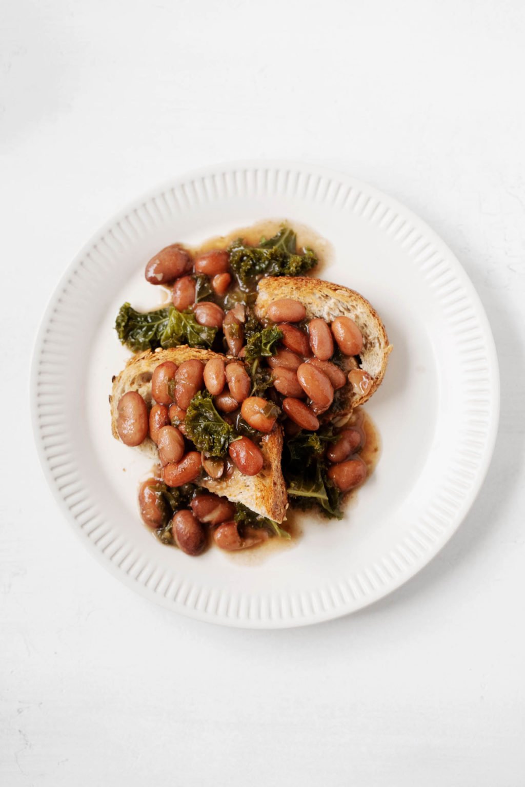 A white, fluted plate holds two slices of toast, cooked leafy greens, and a plant-based protein.