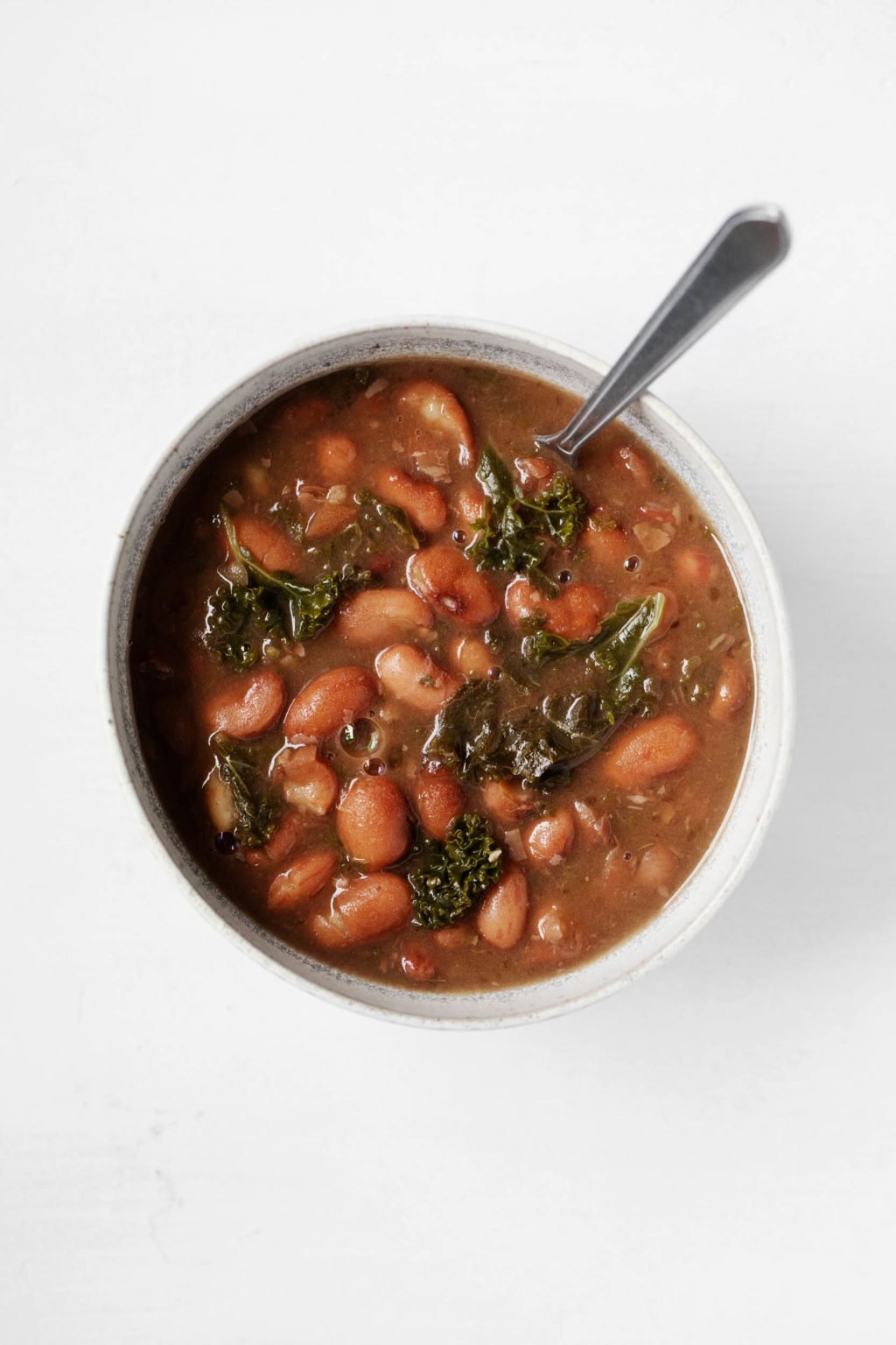 A white bowl is filled with soupy cooked cranberry beans and kale.