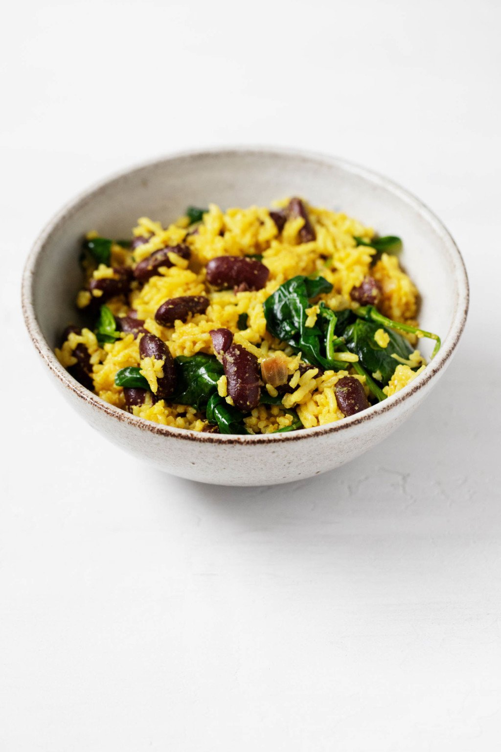 A small, ceramic bowl holds a plant-based meal of kidney beans, whole grains, and spinach.