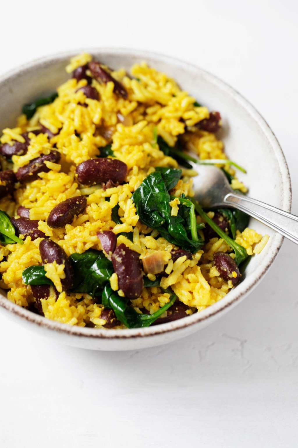 A ceramic bowl holds a golden-hued meal of turmeric rice, beans, and greens.