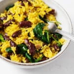 A ceramic bowl holds a golden-hued meal of turmeric rice, beans, and greens.