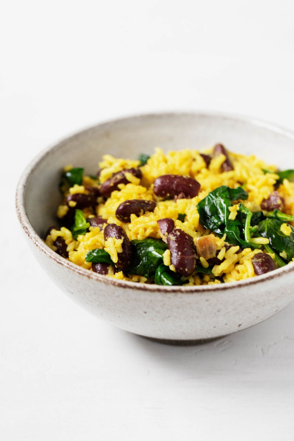 A white serving bowl is filled with a colorful mix of turmeric rice, beans and greens