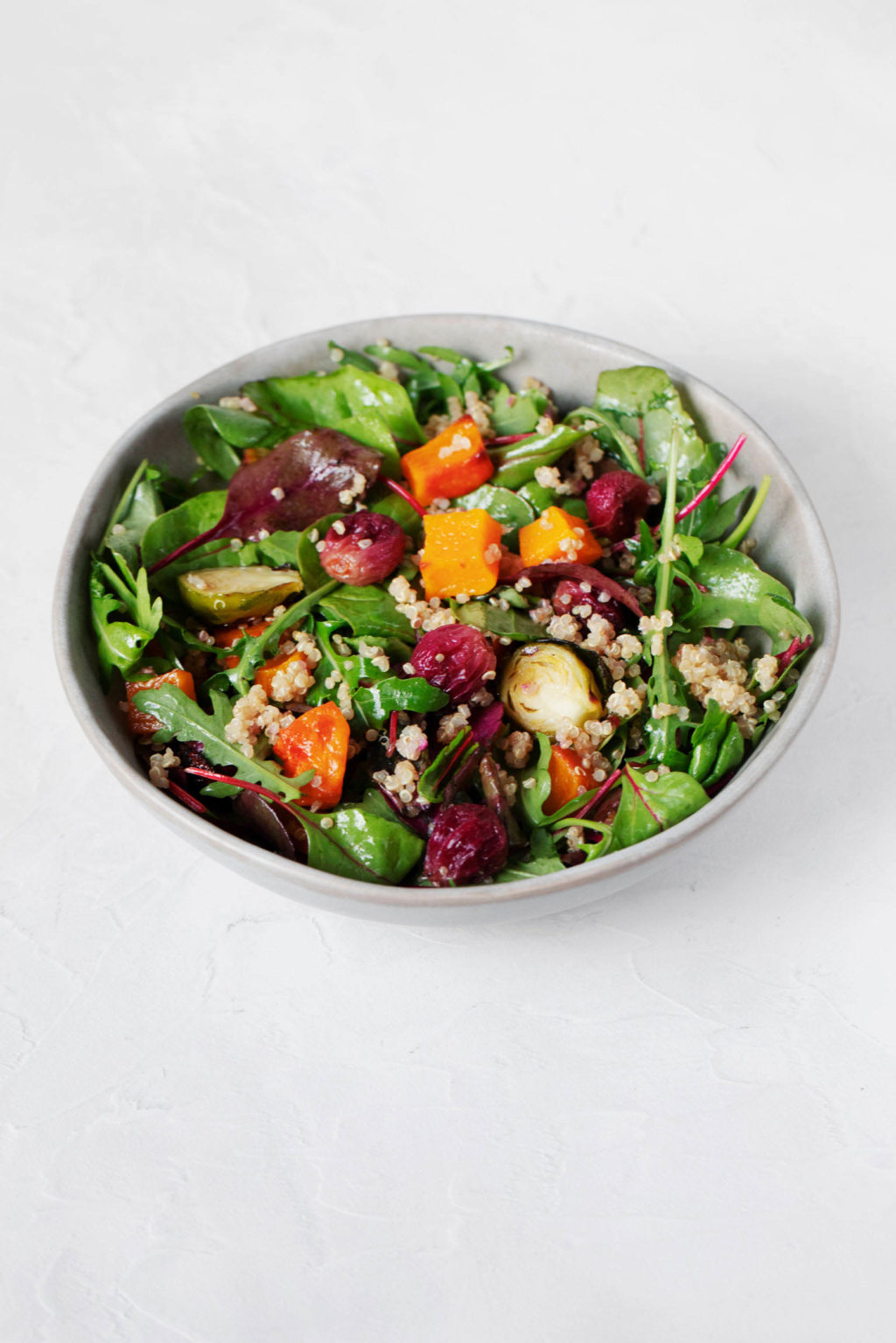 A round salad bowl, captured at a distance on a white surface, holds baby greens and cooked autumn vegetables.