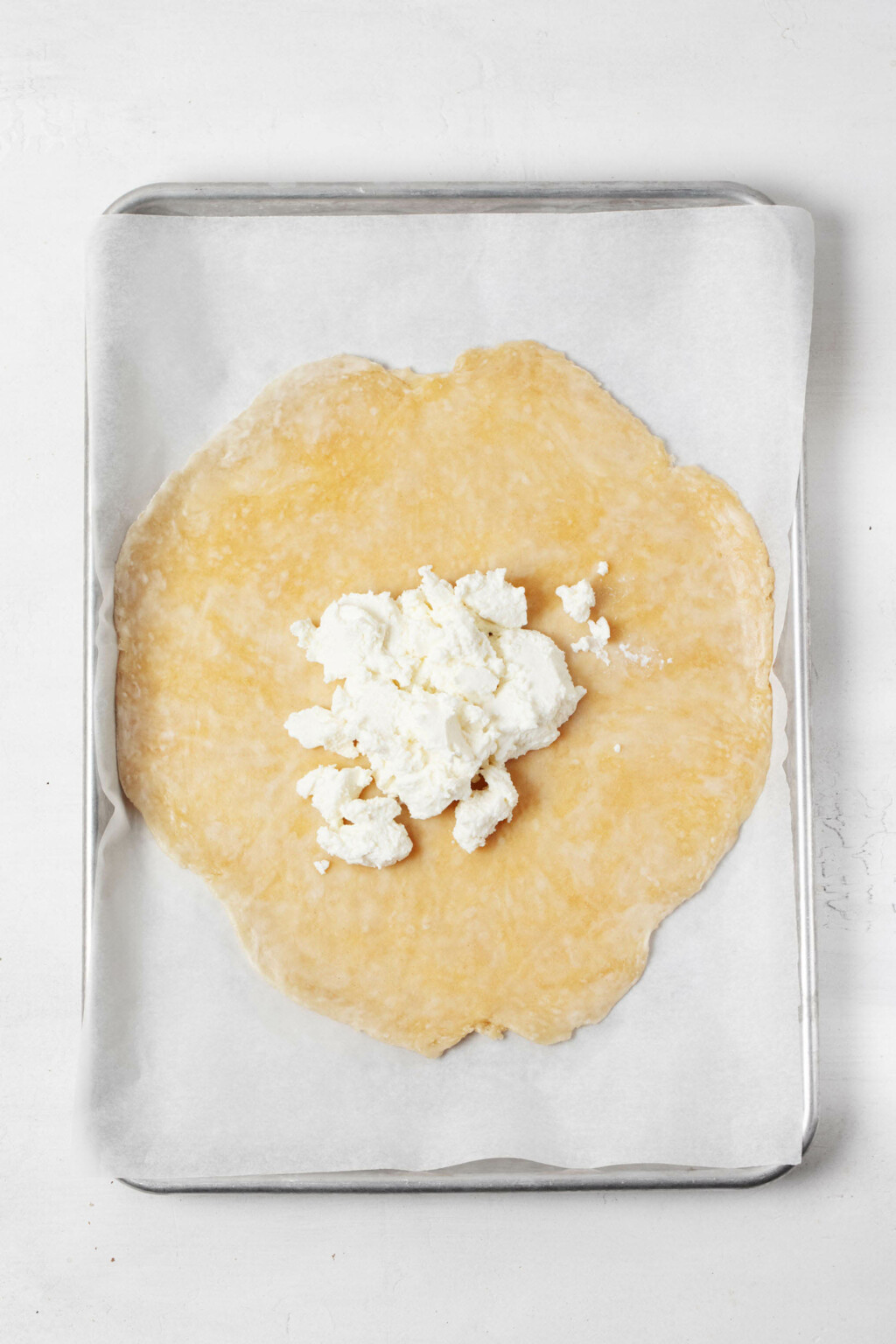 A round of pastry dough is being spread with a light layer of plant-based cheese.