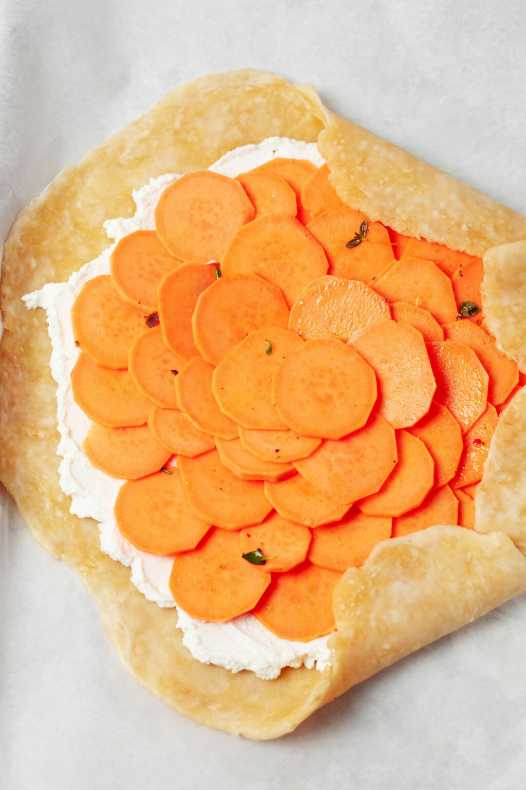 A round of vegan pastry dough is being folded over a layer of cashew cheese and thin rounds of sliced sweet potato.