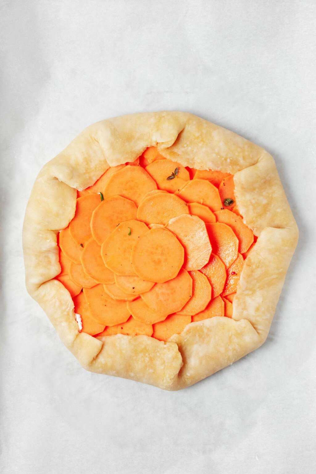 A vegan sweet potato galette is being prepared on a sheet of white parchment paper.
