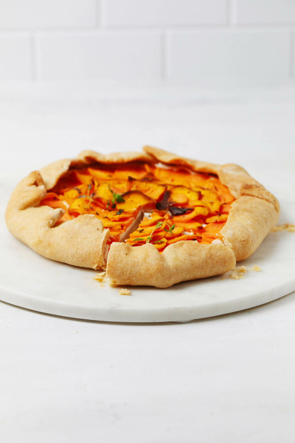 An angled shot of a savory pastry made with sweet potatoes, which is resting on a white marble serving round.