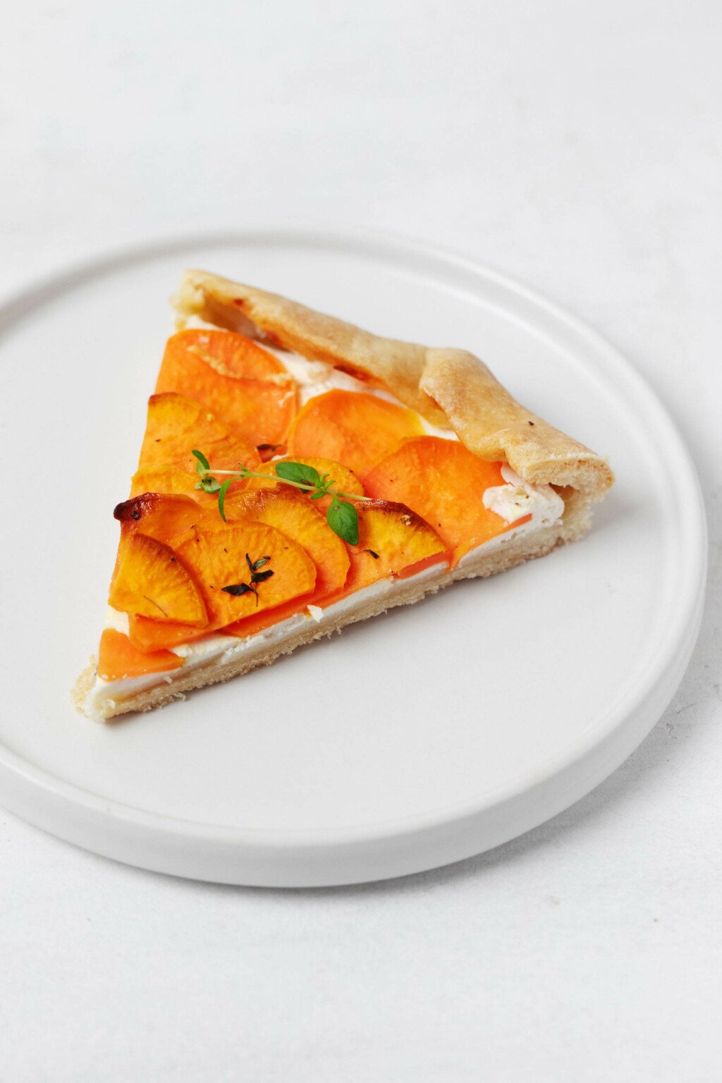A triangular slice of a vegan galette, which is made with sweet potatoes and cashew cheese, is resting on a small, white plate.