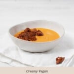 An asymmetrical, round bowl is resting on a light linen cloth. The bowl contains a creamy vegan butternut squash soup.