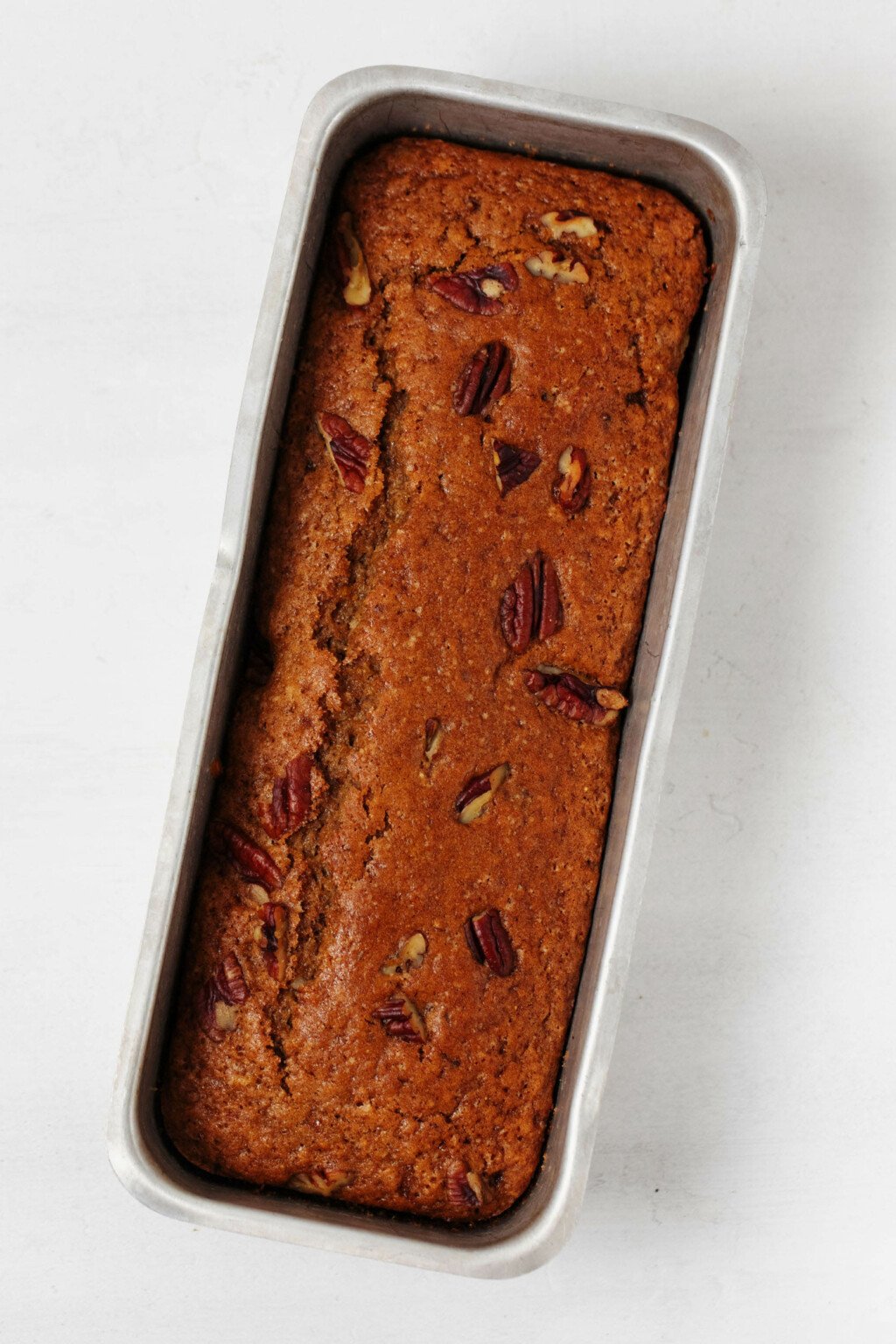 A metal baking loaf has recently been used to prepare a vegan quick bread. The bread is studded with pieces of pecan.