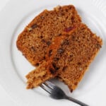 A moist, fluffy vegan pecan citrus loaf has been sliced and plated. A fork is being used to cut into one slice.
