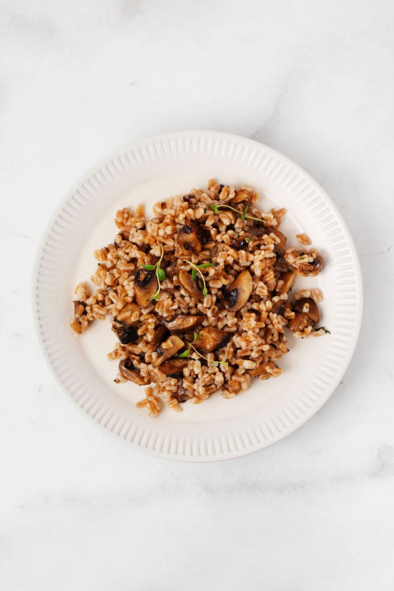 A dish of whole grain farro and mushrooms is on a white, fluted plate.