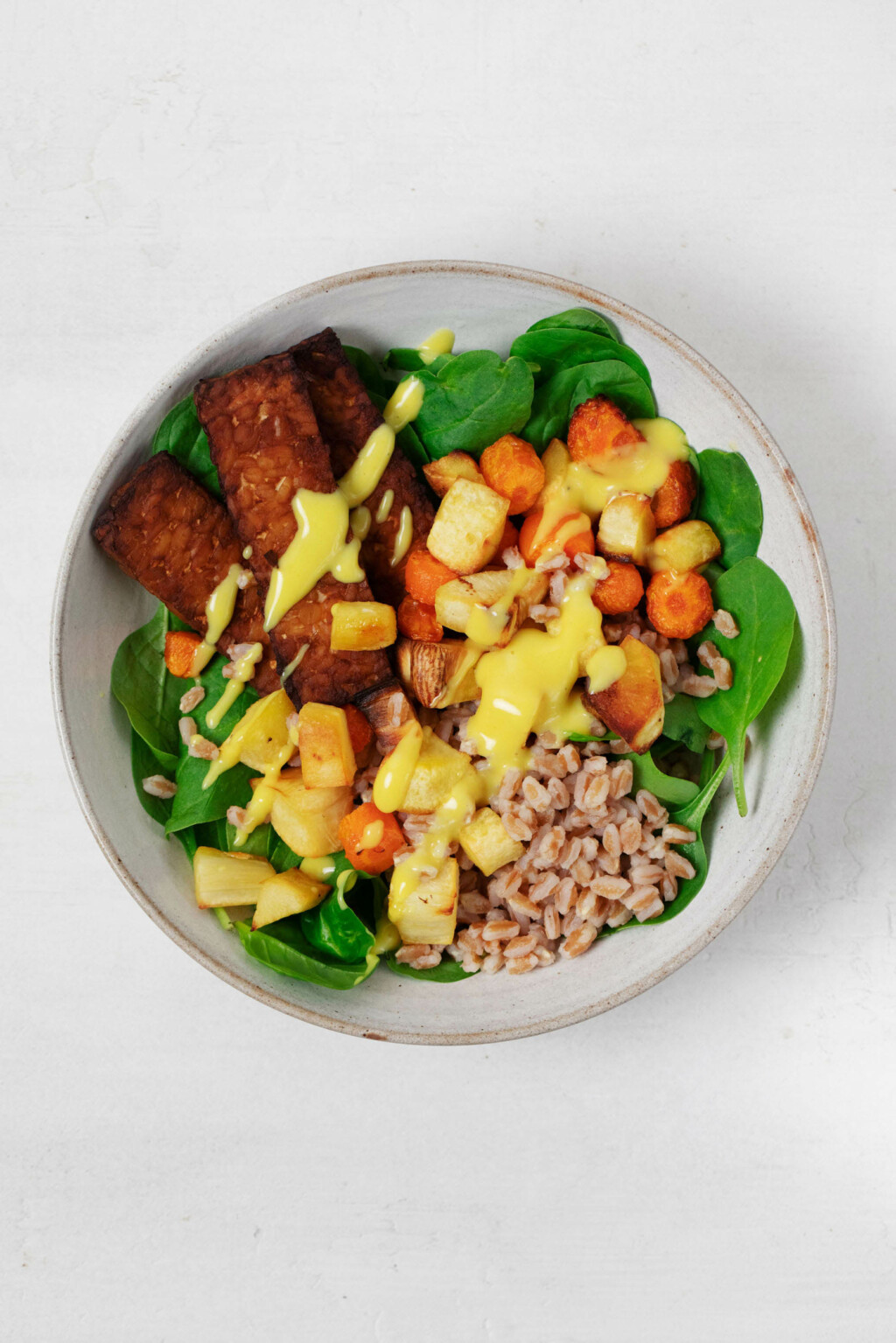 A vegan grain bowl has been piled into a round, white ceramic dish.