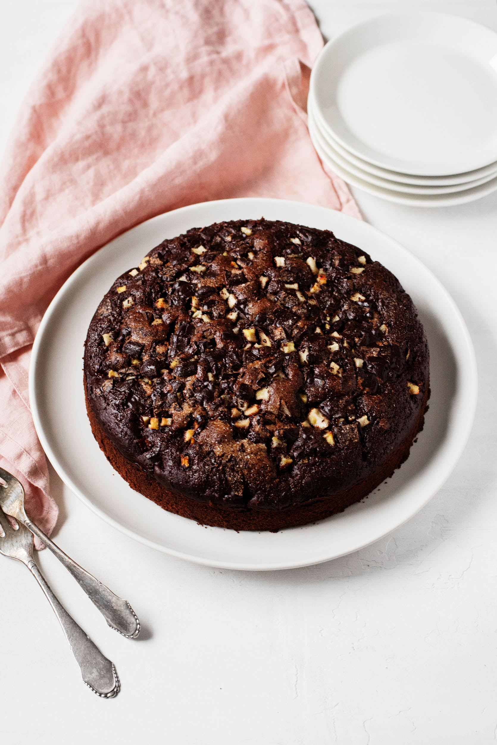 A round chocolate cake is ready to be served, with a stack of small dessert plates nearby.
