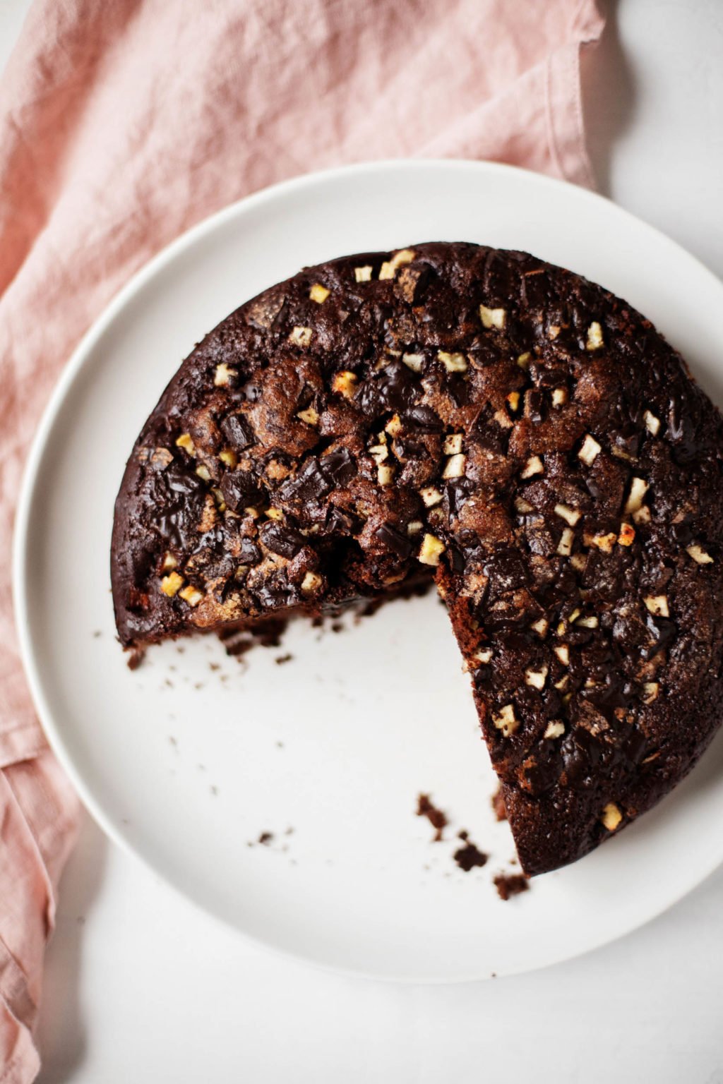 A few slices have been cut out of a round, chocolate cake, which rests on a serving dish.