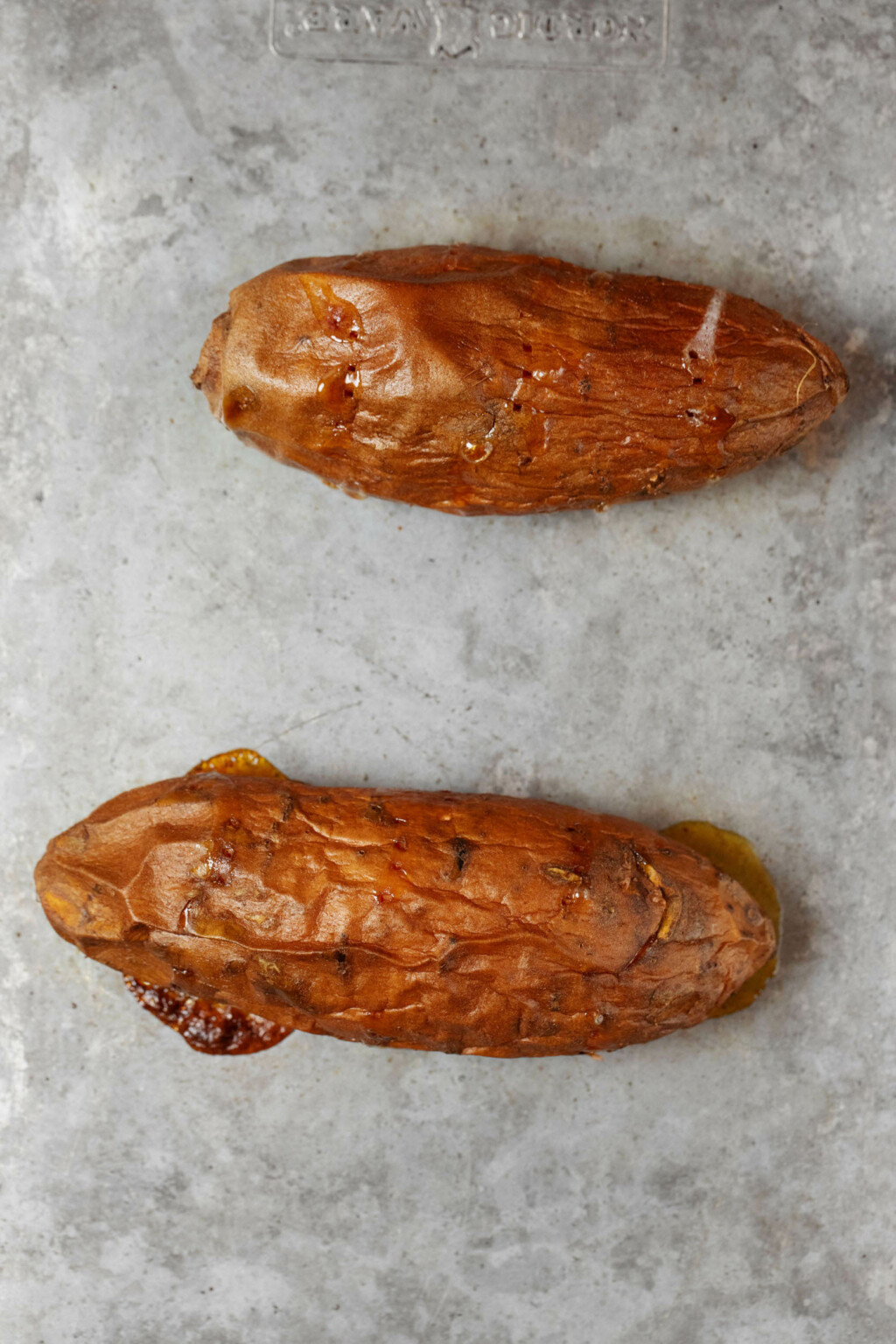An overhead image of two baked sweet potatoes on a white parchment-lined sheet.