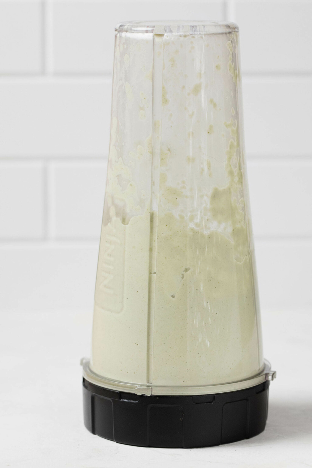 A sideways image of a personal sized blender, which is being used to whip up a pale green pumpkin seed cream.
