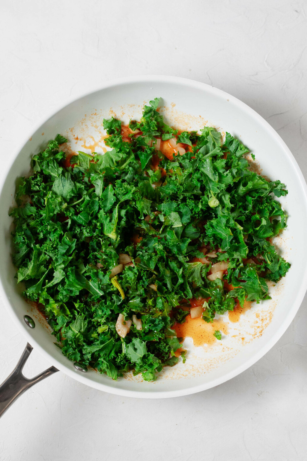 A white skillet is being used to sauté bright green, chopped curly kale.