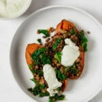 An overhead image of a stuffed sweet potato, which has lentils and bright green kale. It's topped with a pumpkin seed cream that's also pictured in a small bowl near the potato.