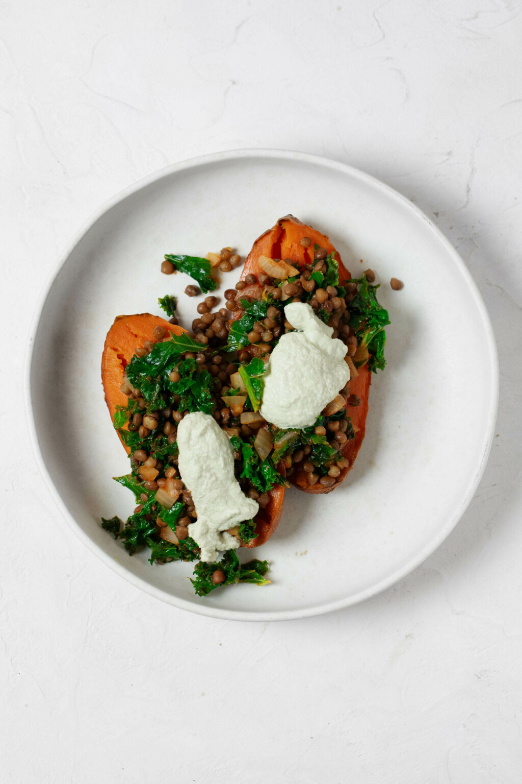 An overhead image of a stuffed sweet potato, which has lentils and bright green kale. It's topped with a pumpkin seed cream.