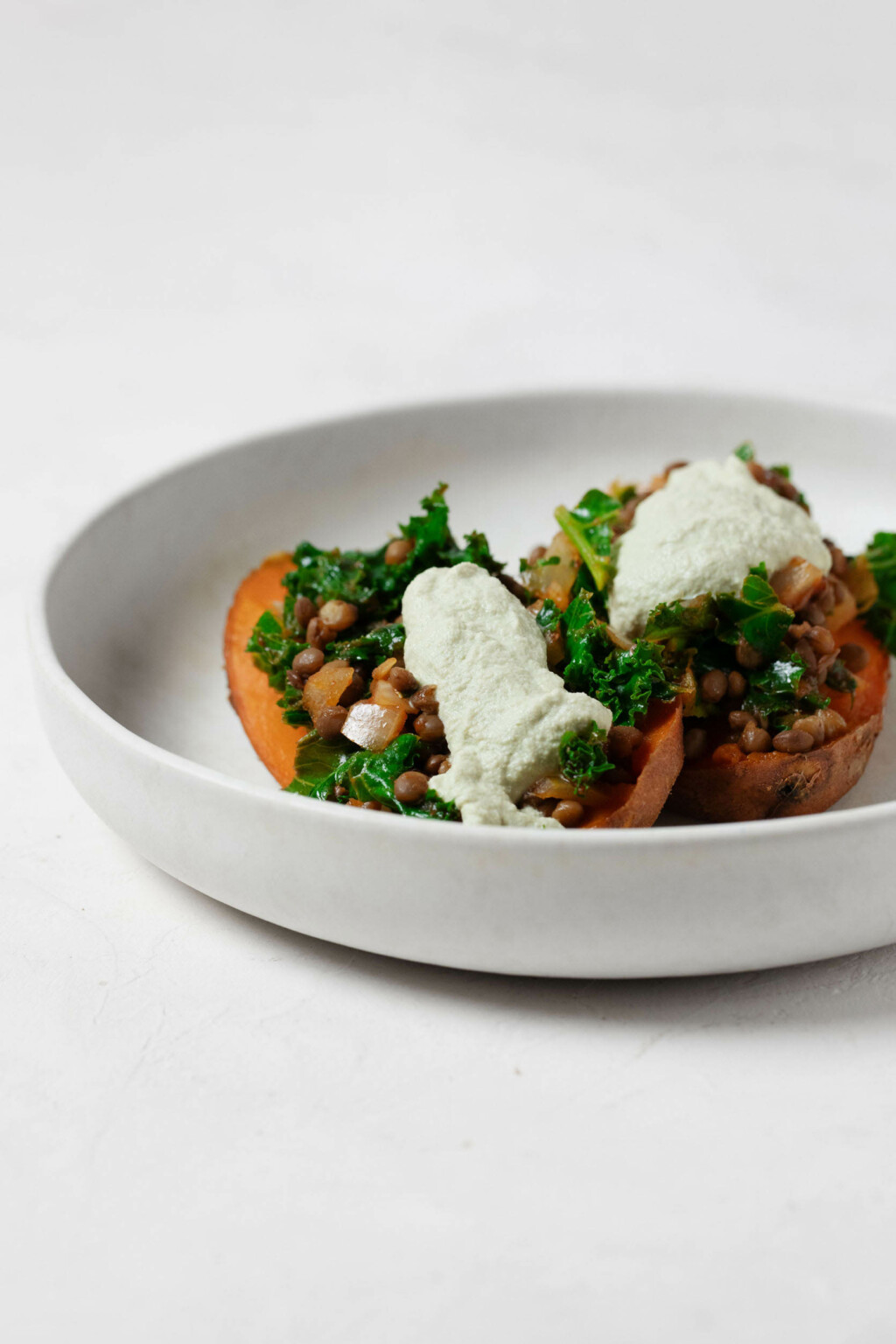 An image of two kale and lentil stuffed sweet potatoes, which are being served in a shallow, white ceramic bowl.