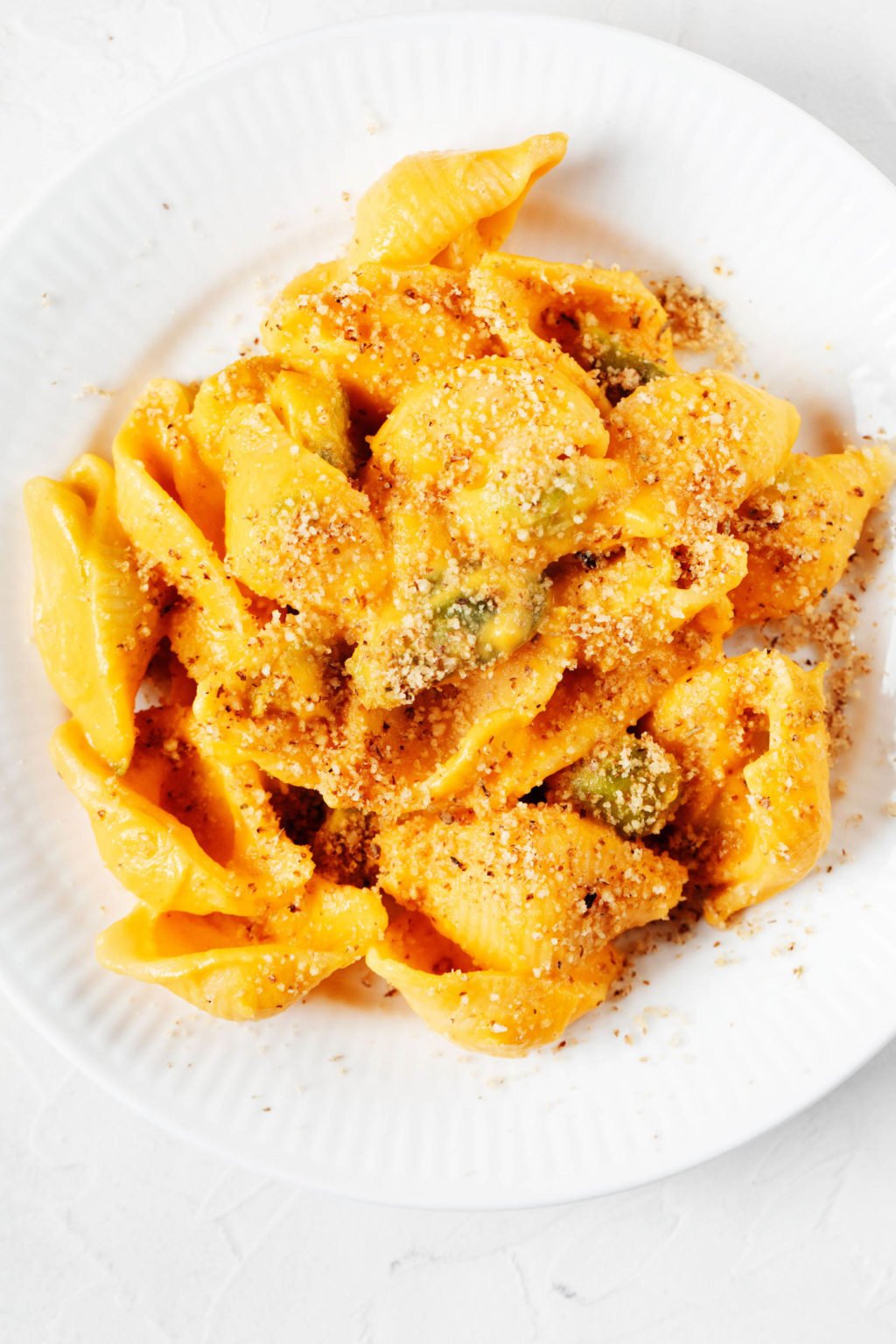 An overhead image of a white, rimmed plate, which has been topped with a helping of creamy vegan carrot mac and cheese.