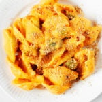 An overhead image of a white, rimmed plate, which has been topped with a helping of creamy vegan carrot mac and cheese.