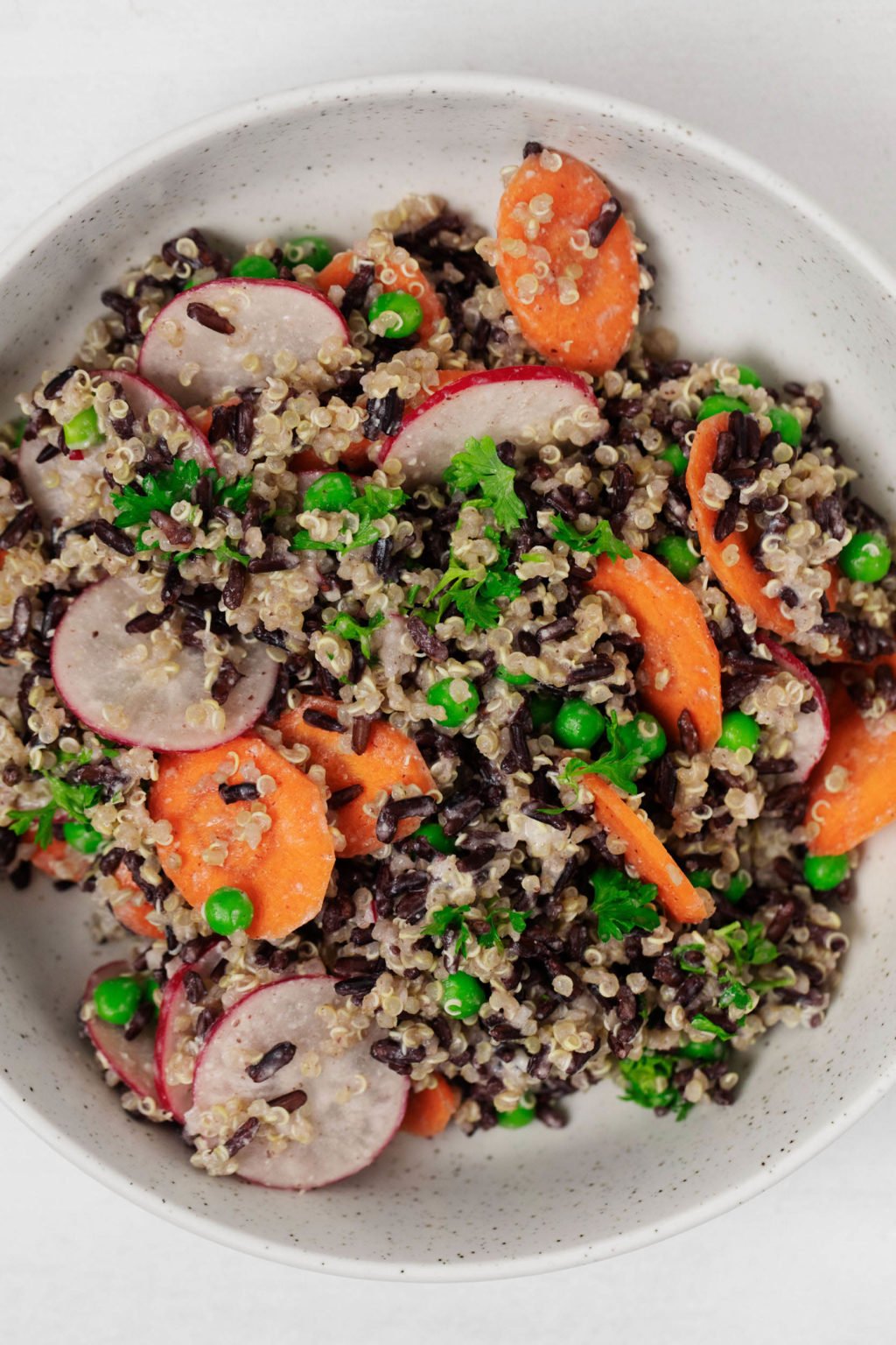 A creamy black rice and quinoa salad with spring peas is served in a white bowl.