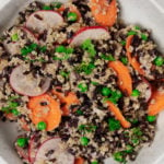 A creamy black rice and quinoa salad with spring peas is served in a white bowl.