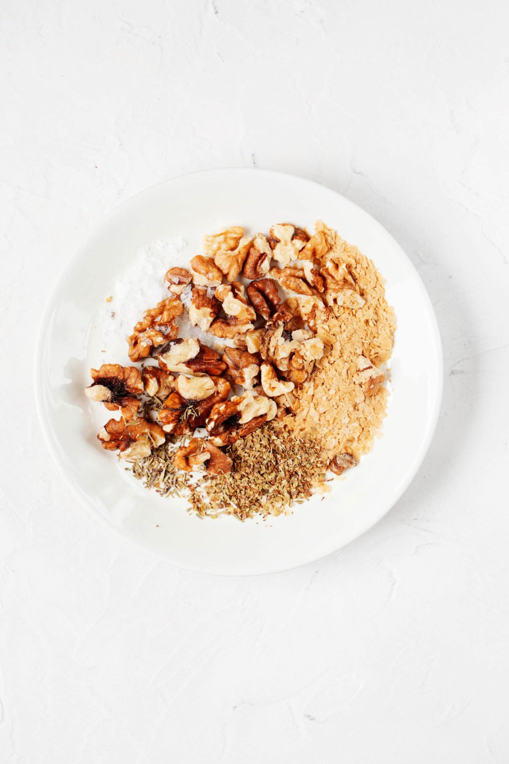 An overhead image of a pinch bowl, which is holding raw walnuts and herbs.