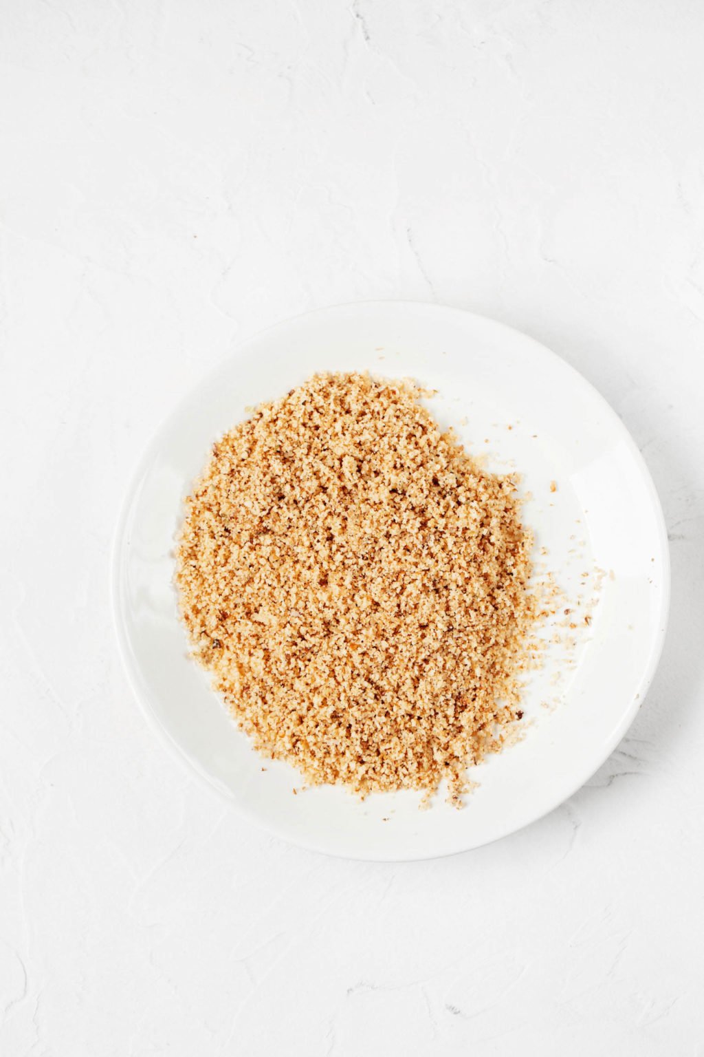 An overhead image of a small, white plate with a ground, nutty topping.