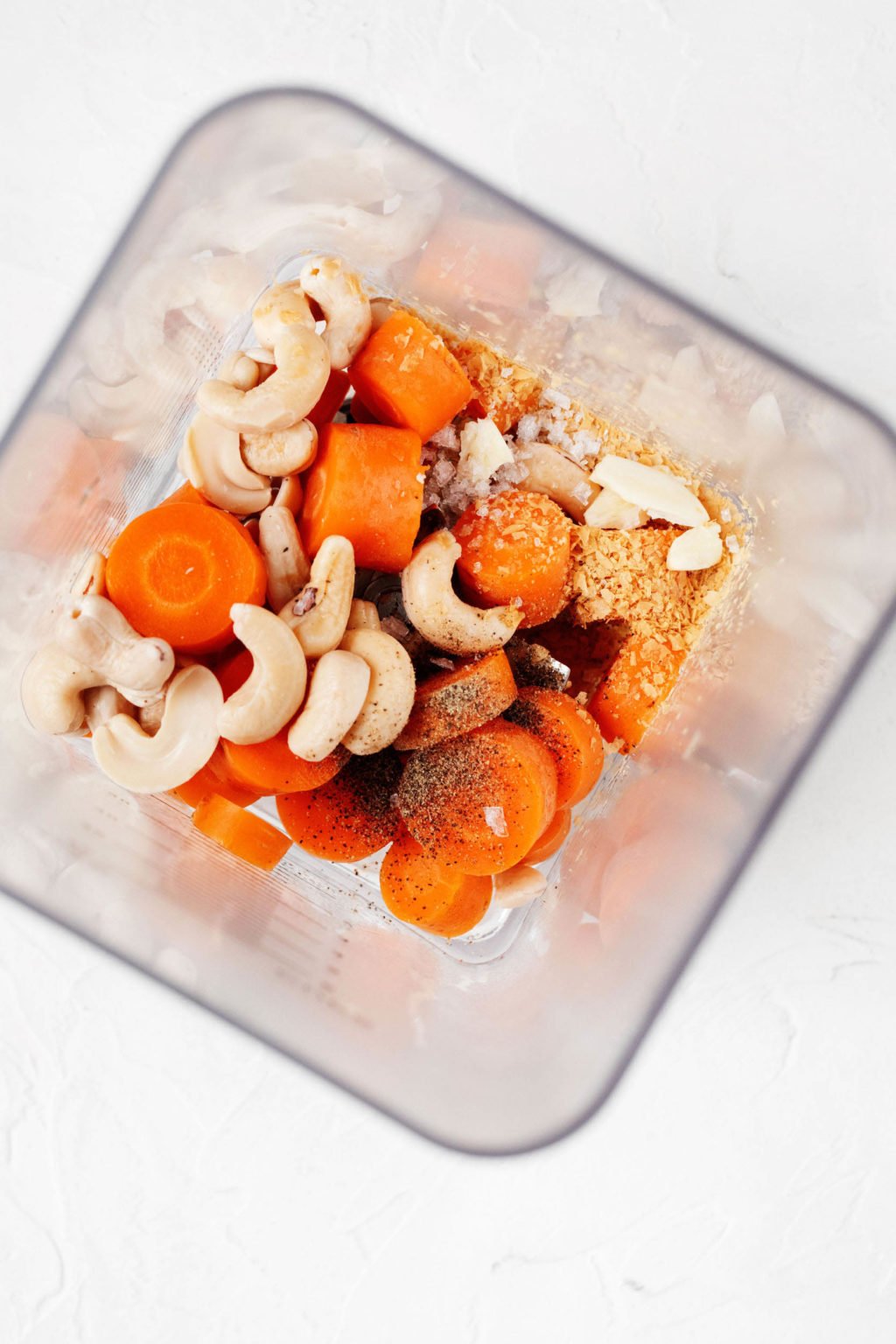 An overhead image of the container of a blender. It's filled with carrots, cashews, and various seasonings.
