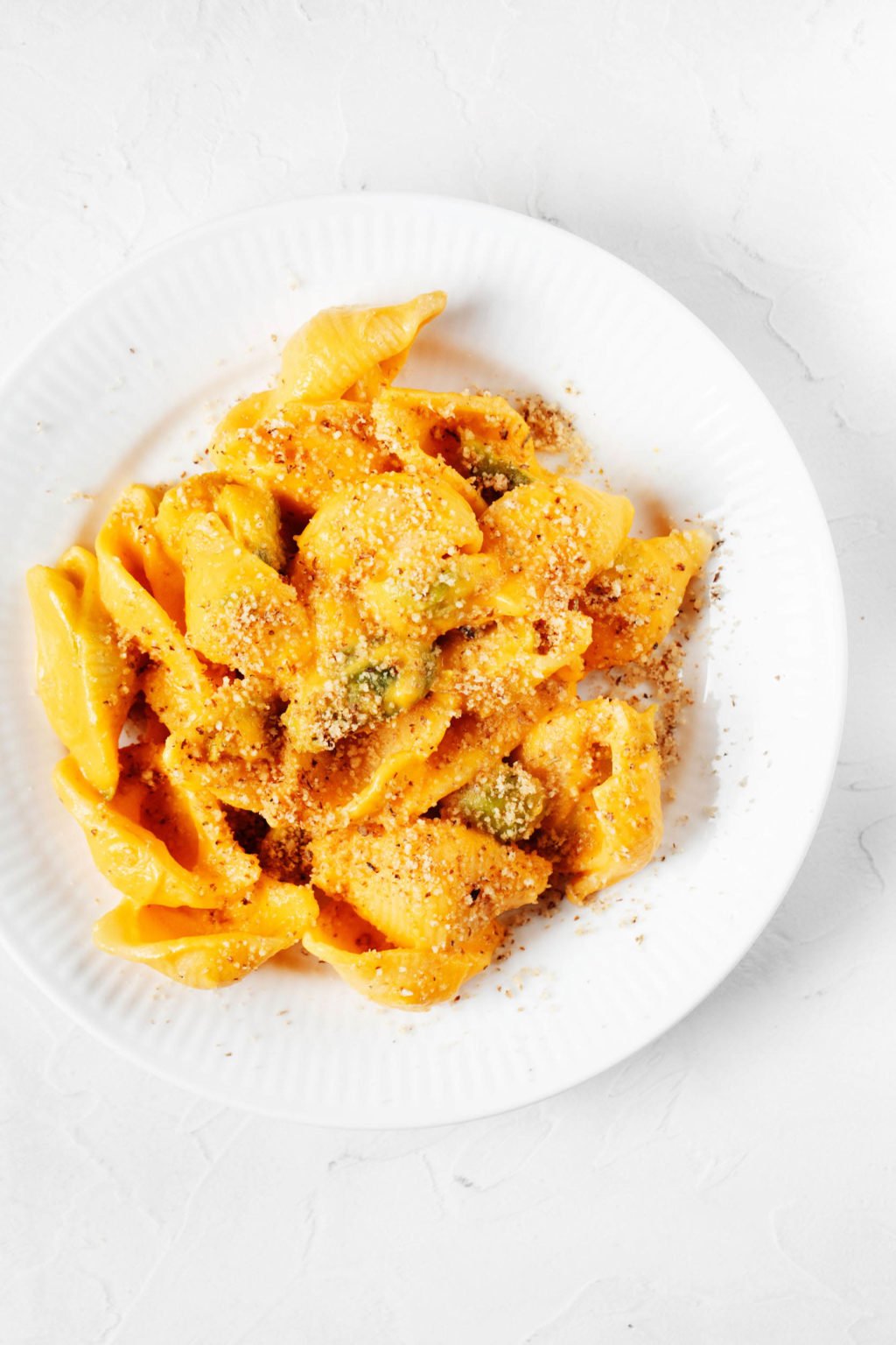 An overhead image of a vegan dish of carrot mac and cheese. It rests in a white plate on a white surface.