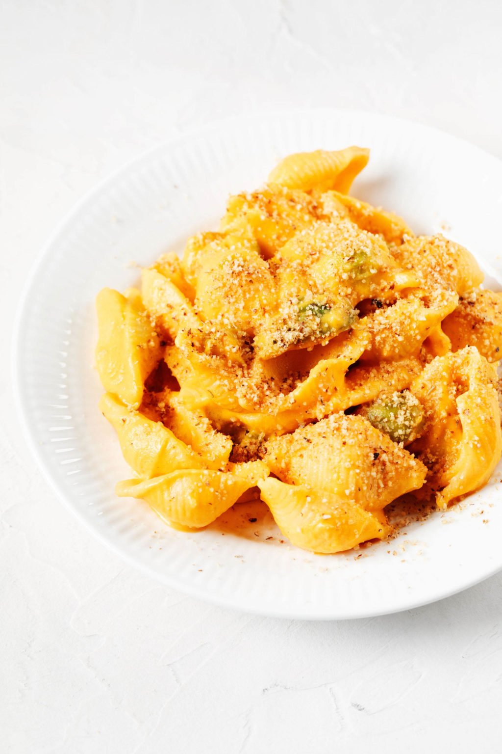 A dish of vibrant orange colored, carrot mac and cheese is resting on a white surface.