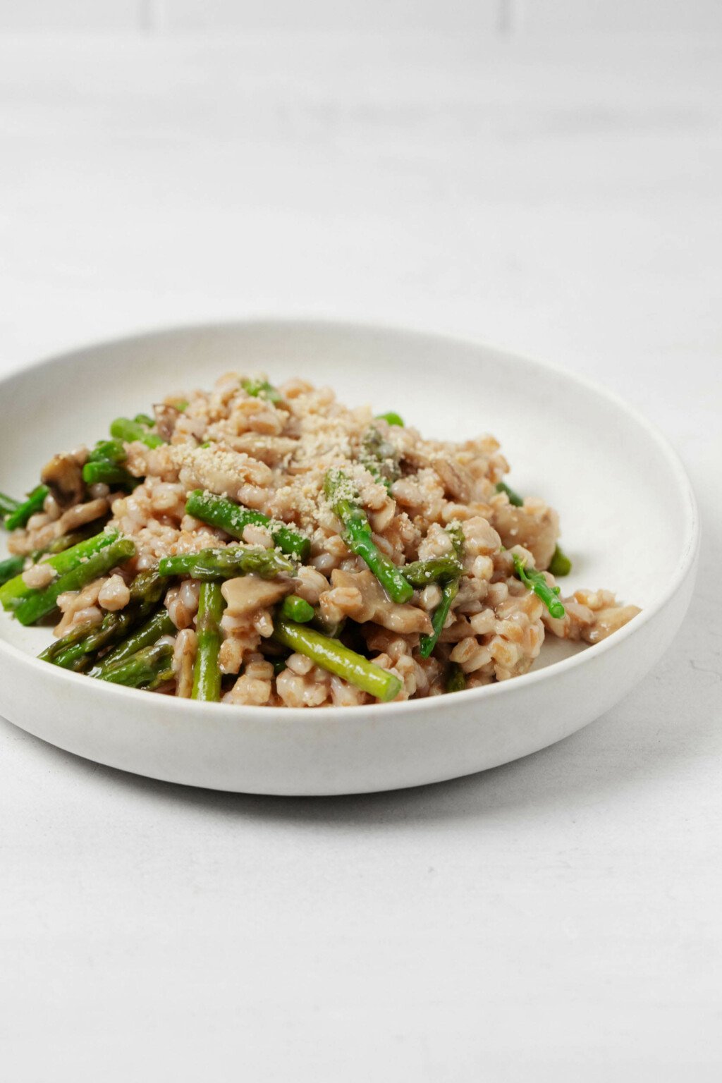 A low, round white bowl holds a whole grain dish with bright green, chopped asparagus spears.