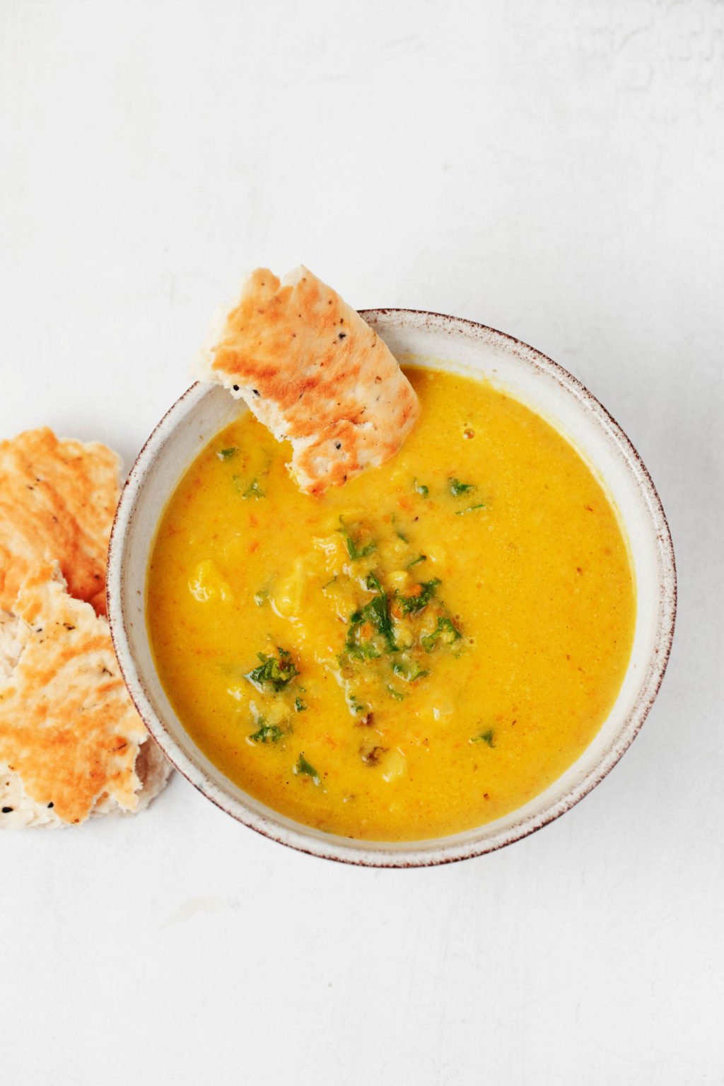 A bowl of golden hued cauliflower kale soup is served with flatbread. It's held in a gray ceramic bowl.