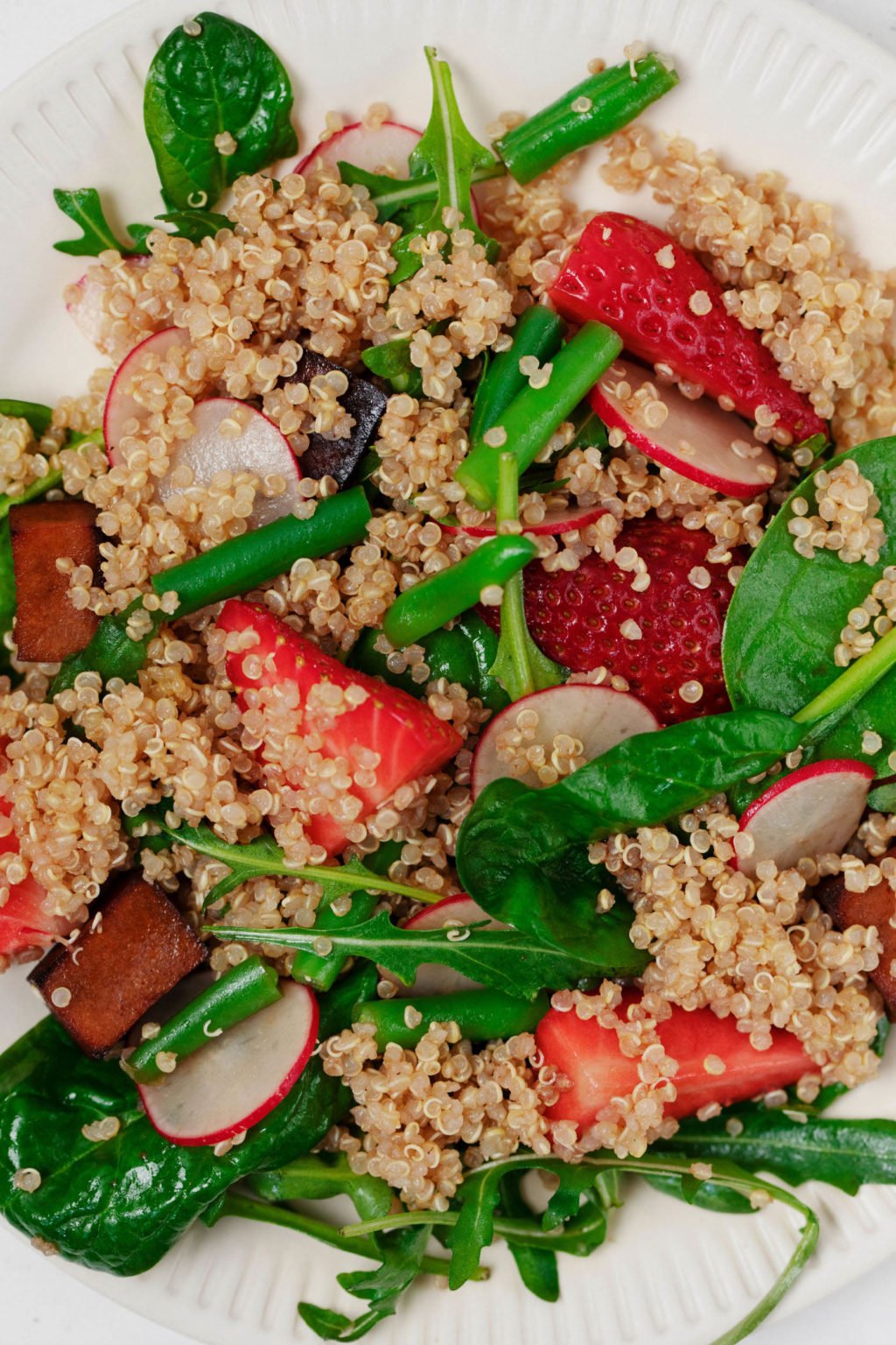 An overhead image of a salad made with tofu, quinoa, strawberries, and baby spinach.