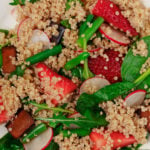 An overhead image of a salad made with tofu, quinoa, strawberries, and baby spinach.