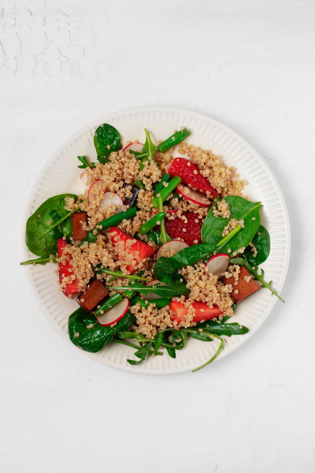 An overhead image of a colorful spring salad with grains, vegetables, and fresh fruit. It's served on a round, white rimmed plate.