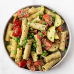 A round, white bowl holds a pasta salad that's made with a tahini base. The pasta salad is full of cherry tomatoes and peas.