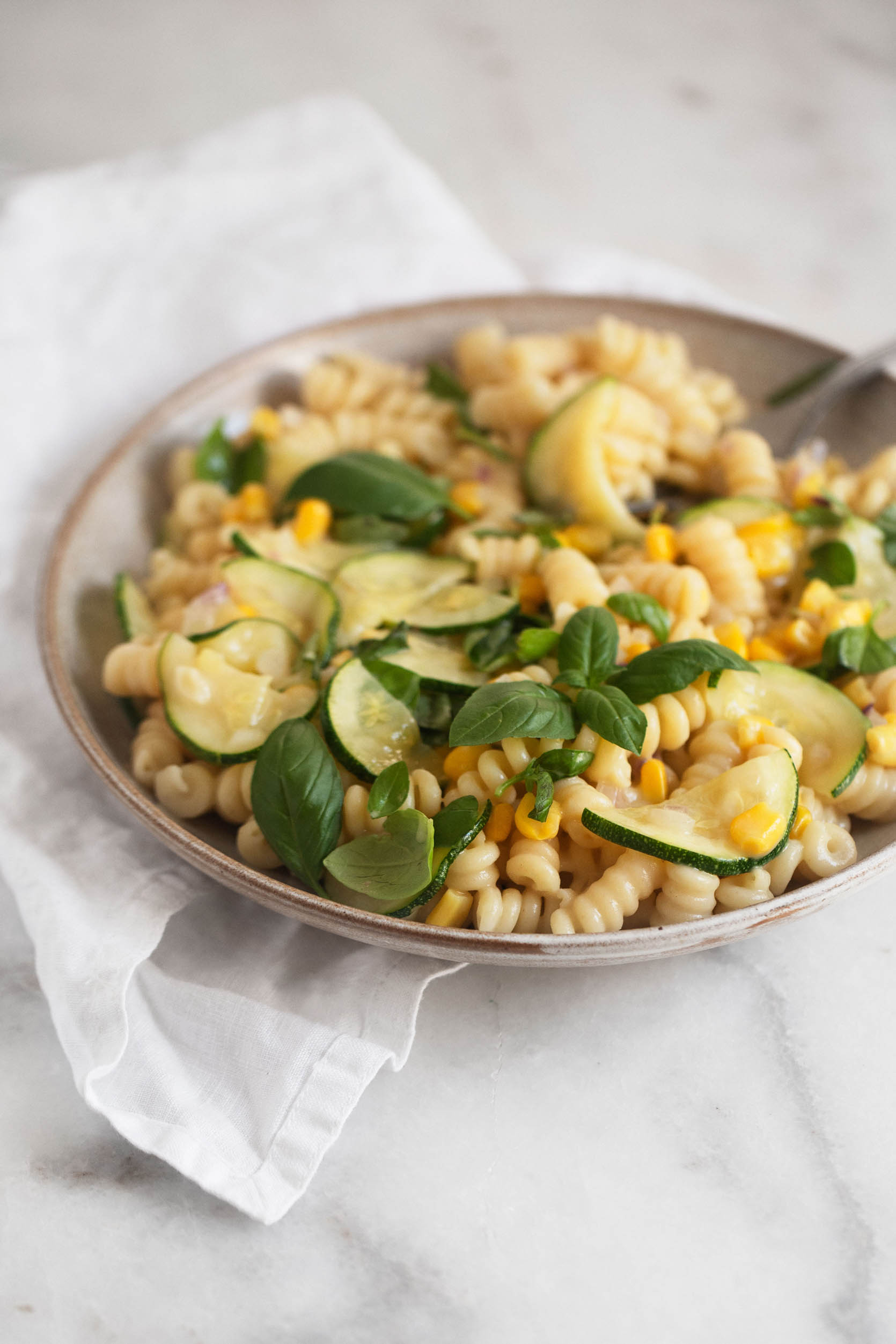 Side angle shot of a vibrant, seasonal, summer pasta with zucchini and corn.