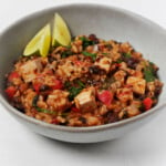 An overhead image of a dish of rice, beans and tofu, with some lime wedges in the bowl.