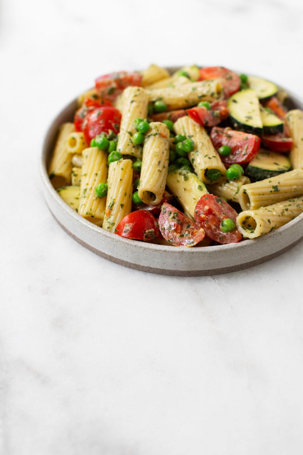 A round, flat plate has been piled high with a plant-based pasta recipe. It rests on a marble surface.